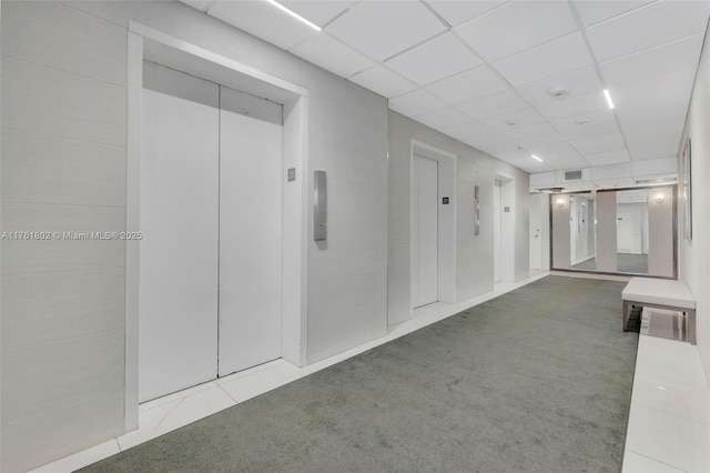 corridor featuring elevator, a drop ceiling, and carpet