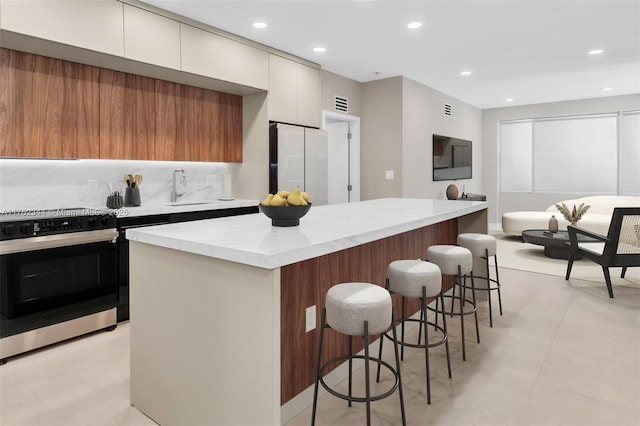 5255 Collins Ave Unit 9B, Miami Beach, FL 33140 - kitchen featuring black range oven, modern cabinets, a sink, a breakfast bar, and a kitchen island
