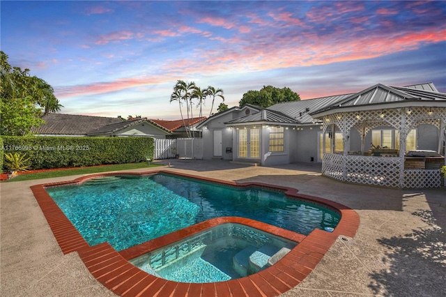 pool at dusk with a patio area, an in ground hot tub, fence, french doors, and a fenced in pool