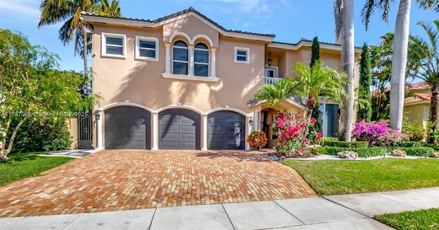 mediterranean / spanish-style home with an attached garage, a tiled roof, stucco siding, driveway, and a gate