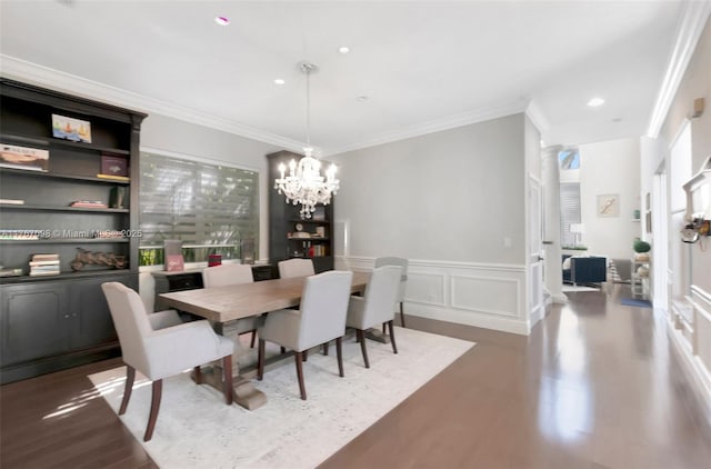 dining space featuring wood finished floors, a wainscoted wall, crown molding, a decorative wall, and a notable chandelier