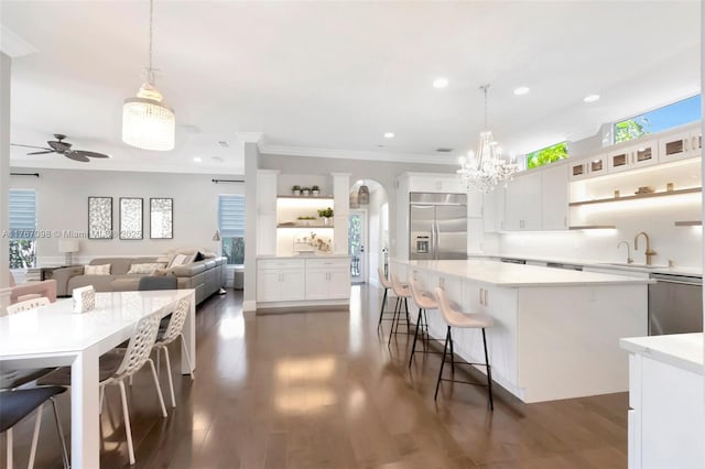 kitchen with open shelves, a sink, stainless steel appliances, a large island, and ceiling fan with notable chandelier