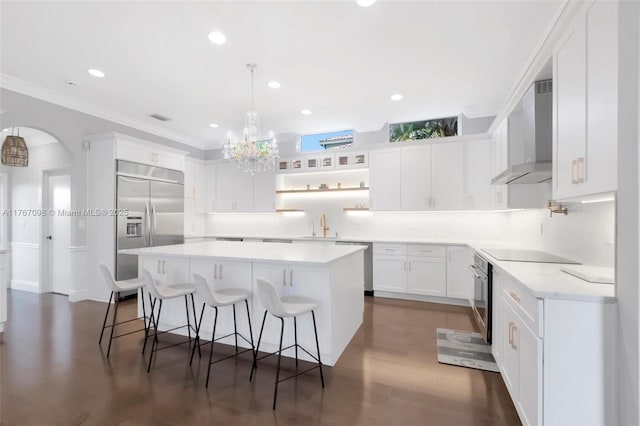 kitchen with wall chimney range hood, a kitchen island, appliances with stainless steel finishes, white cabinetry, and a kitchen breakfast bar