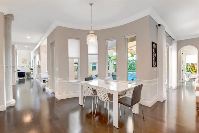 dining room with a wainscoted wall, arched walkways, dark wood-style flooring, crown molding, and a decorative wall