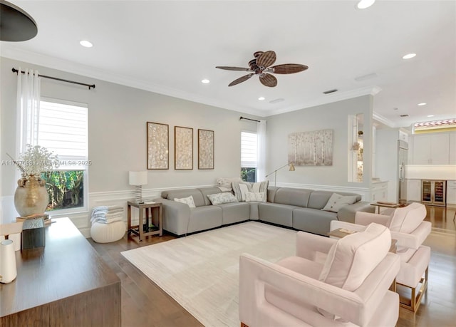 living area with wainscoting, crown molding, ceiling fan, and wood finished floors