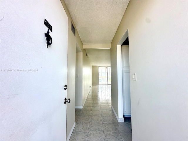 hall with baseboards, a textured ceiling, and visible vents