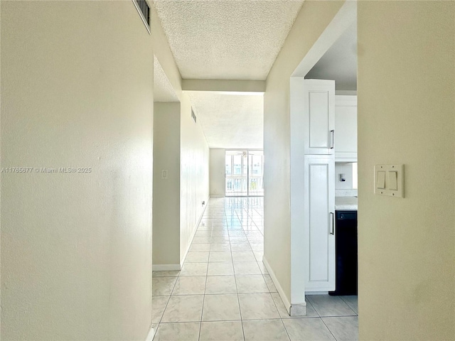 hallway featuring baseboards, visible vents, a textured ceiling, and light tile patterned floors