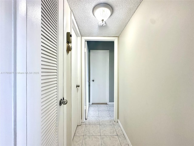 hallway with light tile patterned floors, a textured ceiling, and baseboards