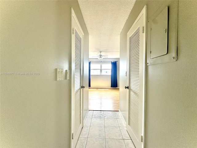 corridor featuring light tile patterned floors, baseboards, electric panel, and a textured ceiling