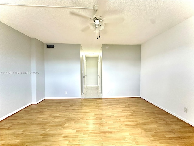 spare room featuring baseboards, a textured ceiling, a ceiling fan, light wood-style floors, and visible vents