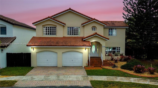 mediterranean / spanish-style home featuring a garage, a tiled roof, stucco siding, and decorative driveway