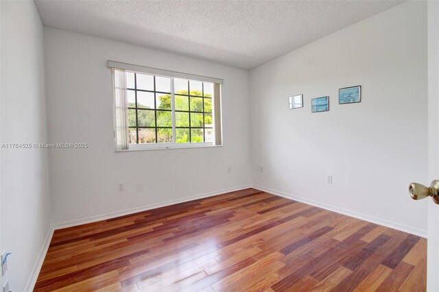 spare room with a textured ceiling, baseboards, and wood finished floors