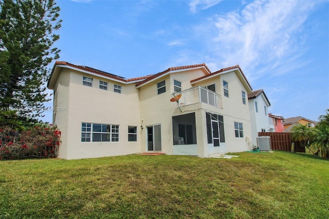 back of house featuring central AC unit, fence, a balcony, a yard, and stucco siding