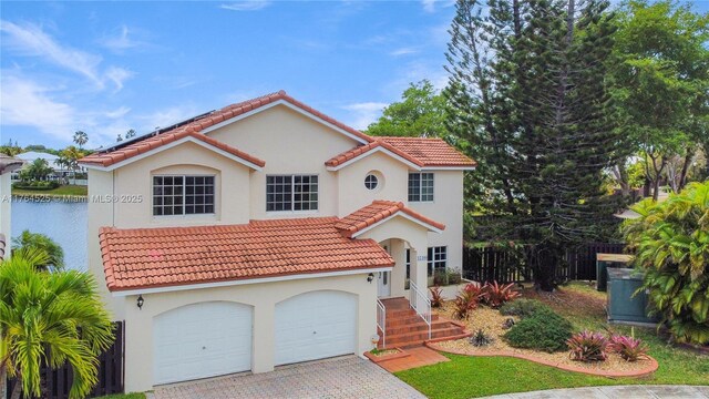 mediterranean / spanish house featuring an attached garage, stucco siding, roof mounted solar panels, decorative driveway, and a tiled roof