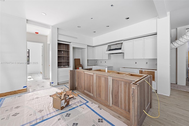 kitchen featuring wall chimney range hood, white cabinets, and a kitchen island