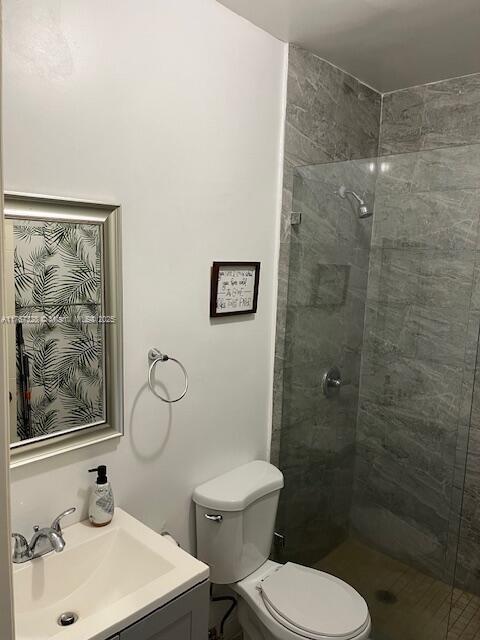 bathroom with toilet, tiled shower, and vanity