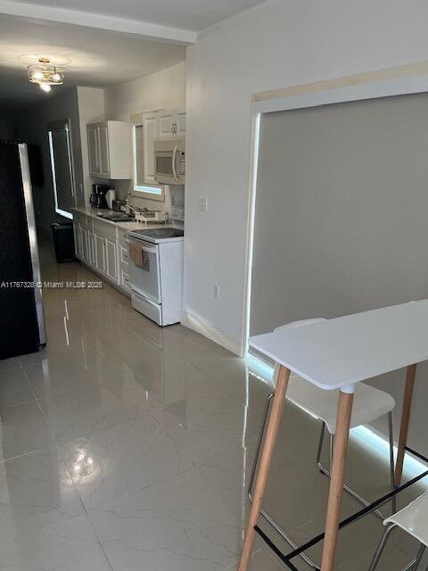 kitchen with freestanding refrigerator, a sink, white cabinets, stainless steel microwave, and white electric range