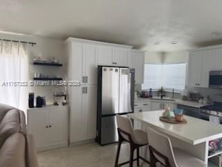 kitchen featuring stainless steel appliances, a kitchen bar, white cabinetry, a sink, and light countertops