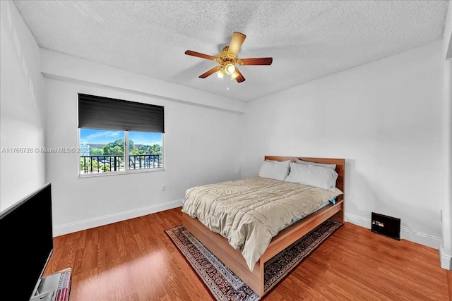 bedroom with a textured ceiling, wood finished floors, baseboards, and ceiling fan
