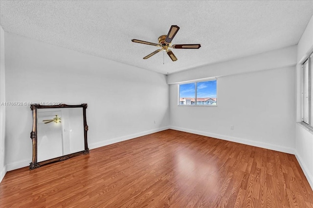 spare room with a textured ceiling, ceiling fan, wood finished floors, and baseboards