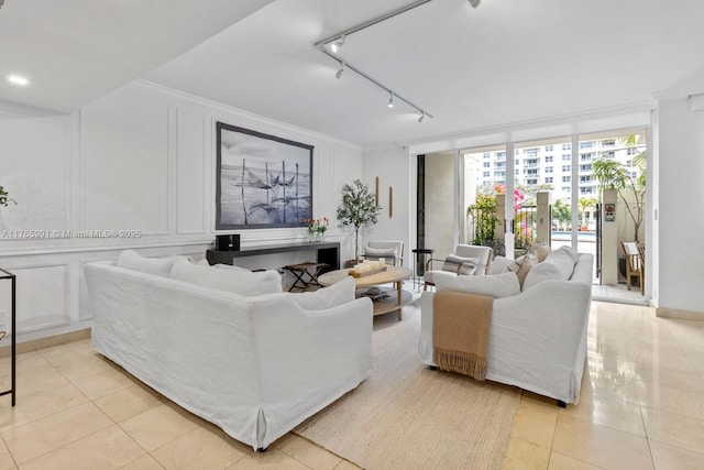 living area featuring a decorative wall, light tile patterned flooring, rail lighting, ornamental molding, and a wall of windows