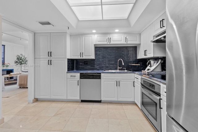 kitchen with stainless steel appliances, a sink, backsplash, under cabinet range hood, and dark countertops