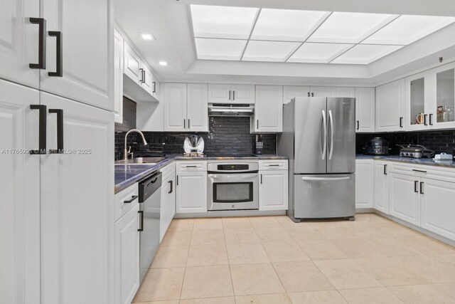 kitchen featuring appliances with stainless steel finishes, under cabinet range hood, a sink, tasteful backsplash, and white cabinets