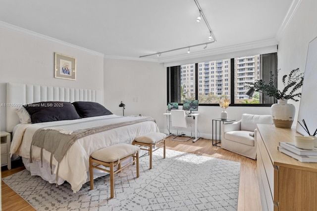 bedroom featuring rail lighting, light wood finished floors, ornamental molding, and baseboards