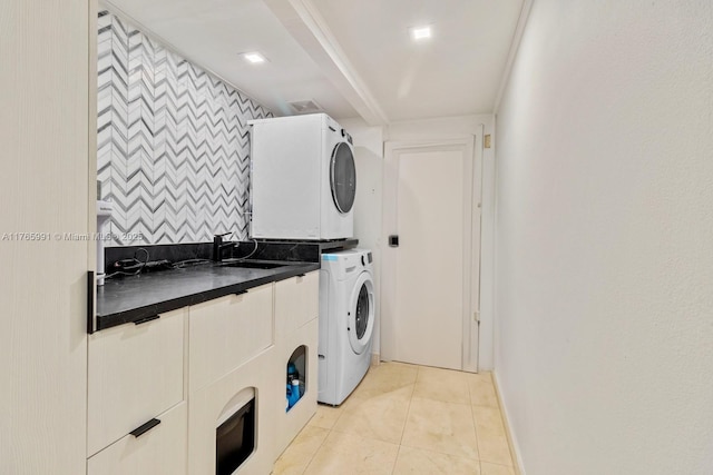 laundry area featuring stacked washer and clothes dryer, cabinet space, light tile patterned floors, and baseboards