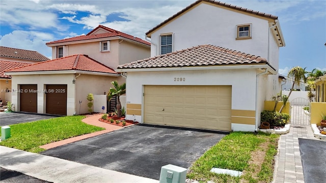 mediterranean / spanish-style house with an attached garage, stucco siding, a gate, a tiled roof, and driveway