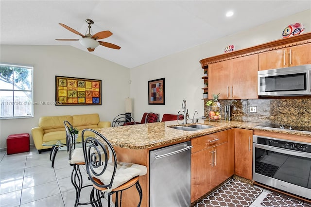 kitchen featuring lofted ceiling, a sink, a peninsula, open floor plan, and stainless steel appliances