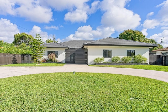 view of front of house with curved driveway, fence, a tile roof, a front yard, and stucco siding