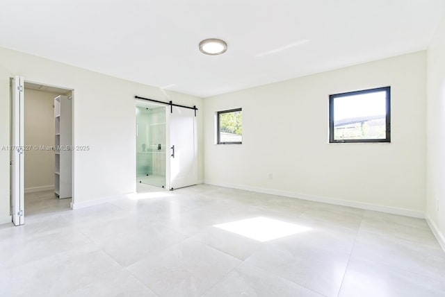 unfurnished bedroom featuring a barn door, a spacious closet, and baseboards