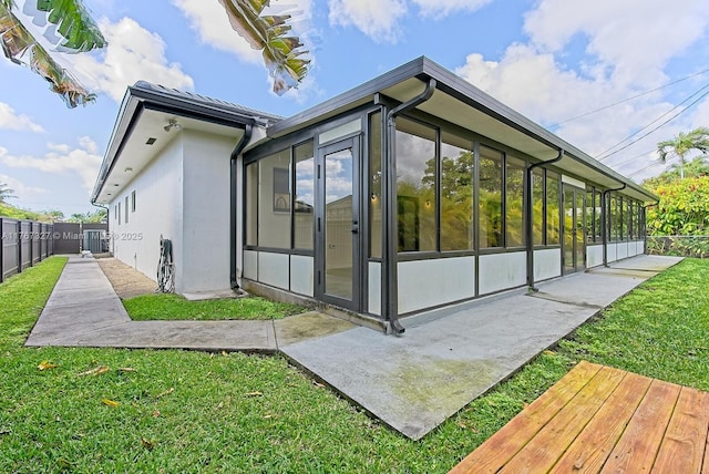 view of home's exterior featuring stucco siding, fence, a yard, and a sunroom