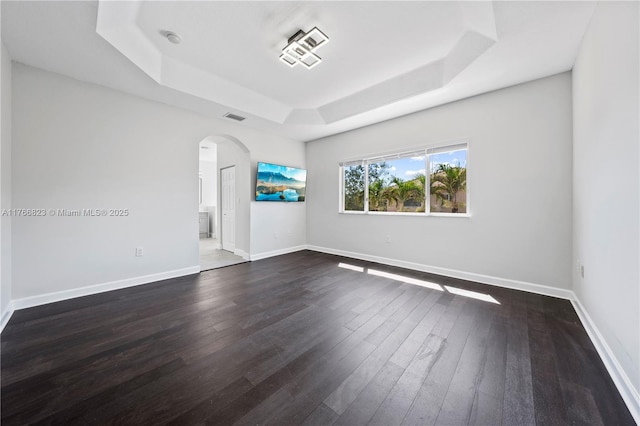 empty room featuring visible vents, a raised ceiling, dark wood-type flooring, arched walkways, and baseboards