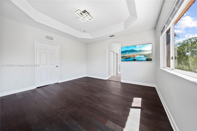 unfurnished room with a tray ceiling, arched walkways, visible vents, and dark wood-style floors