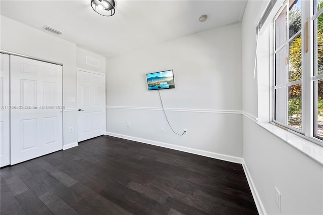 unfurnished bedroom featuring a closet, visible vents, dark wood-type flooring, and baseboards