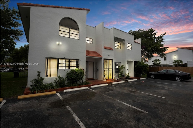 view of front of house with stucco siding, a tiled roof, fence, and uncovered parking