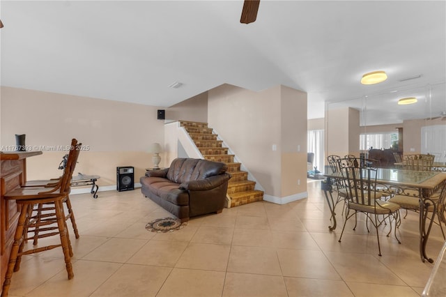 living area with light tile patterned floors, baseboards, a ceiling fan, and stairs