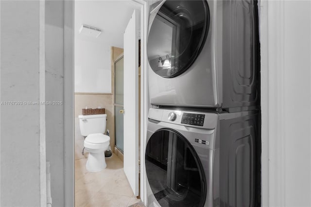 washroom featuring laundry area, stacked washer and dryer, and light tile patterned flooring