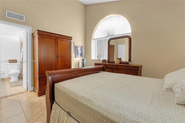 bedroom featuring light tile patterned floors, visible vents, ensuite bathroom, and a high ceiling