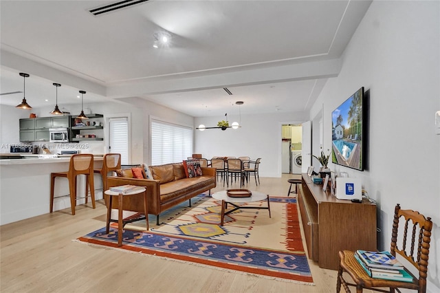 living area featuring light wood-type flooring, visible vents, washer / dryer, and an inviting chandelier