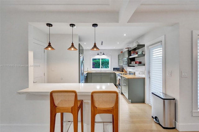 kitchen featuring light countertops, appliances with stainless steel finishes, a sink, green cabinetry, and open shelves
