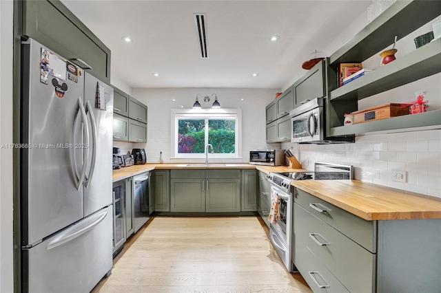 kitchen with green cabinets, tasteful backsplash, butcher block countertops, appliances with stainless steel finishes, and light wood-style flooring