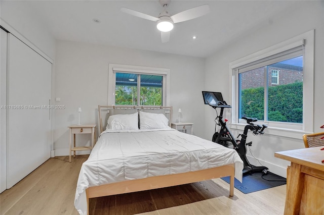 bedroom featuring a ceiling fan, baseboards, multiple windows, and light wood finished floors