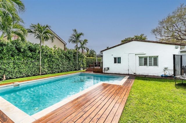 outdoor pool featuring a trampoline, a deck, and a lawn