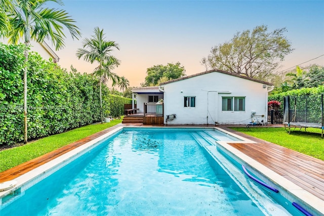 pool featuring a lawn, fence, a trampoline, and a deck