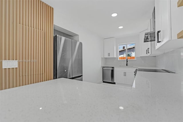 kitchen with light stone countertops, a sink, stainless steel appliances, white cabinets, and tasteful backsplash