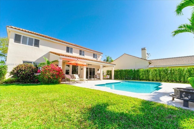 rear view of property with an outdoor pool, ceiling fan, stucco siding, a patio area, and a lawn