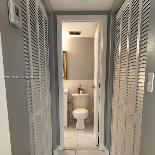 16465 NE 22nd Ave Unit 114, North Miami Beach, FL 33160 - bathroom with tile walls, a wainscoted wall, visible vents, marble finish floor, and toilet